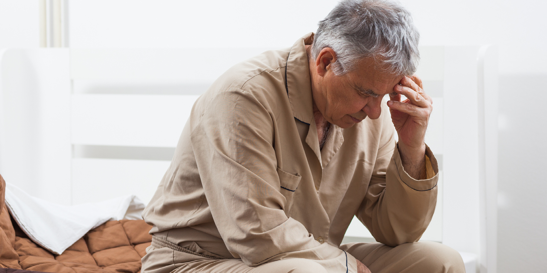 Man sitting on bed in pajamas, head in hand