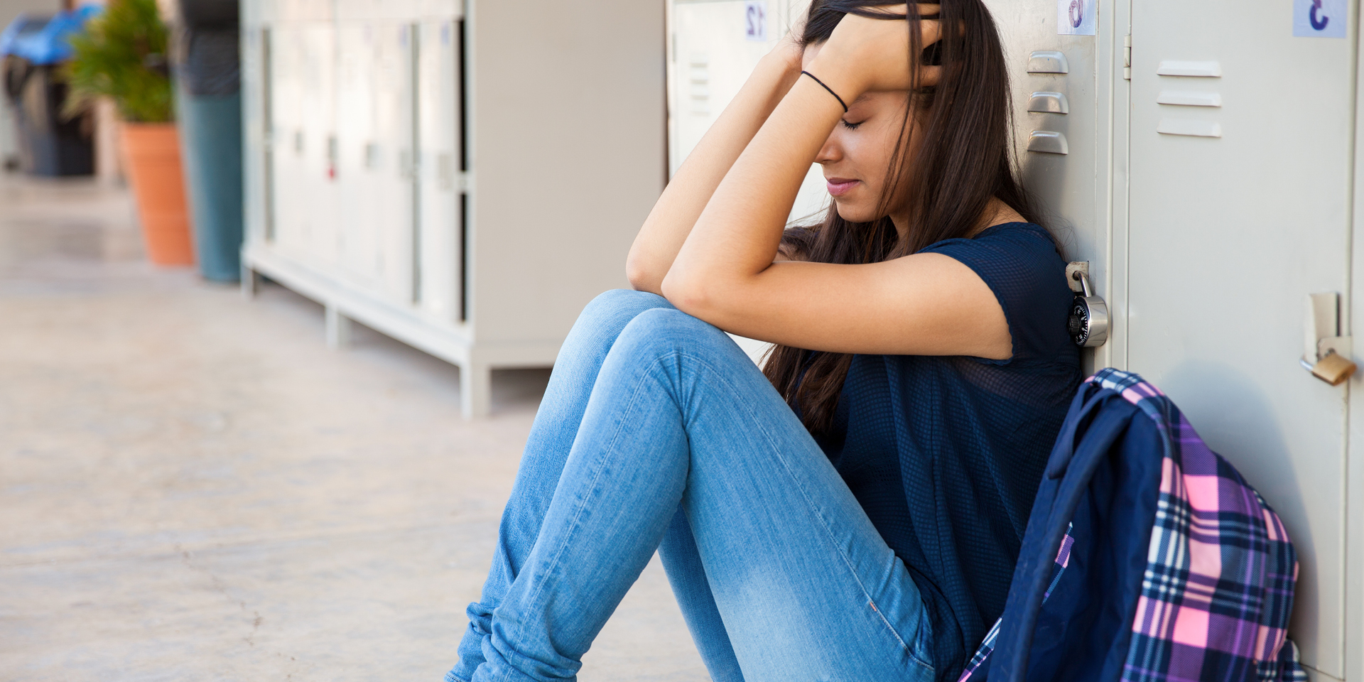 girl sitting, hands in hair, leaning against lockers